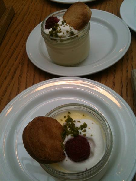 Desserts in glass jars with cream, raspberry, pistachio and cookie, on wooden table