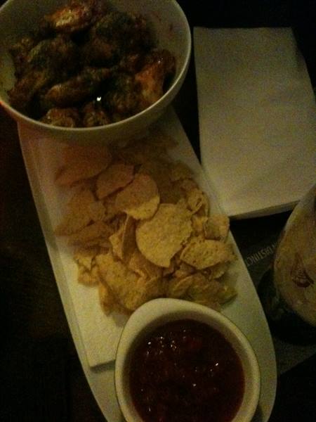 Chicken wings nachos and red salsa served on white platter in dim light