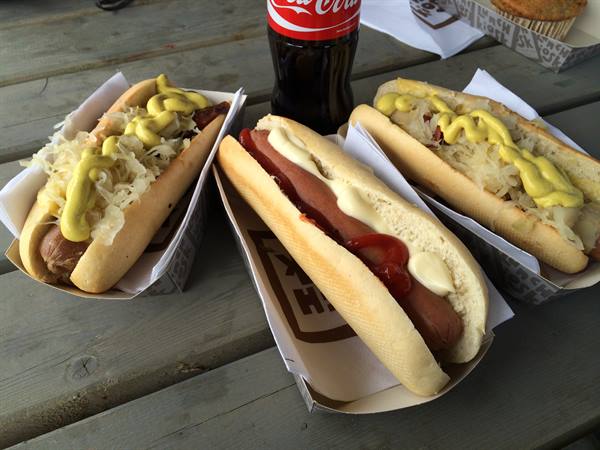 Three hot dogs with mustard and sauerkraut on a wooden table, with Coca-Cola