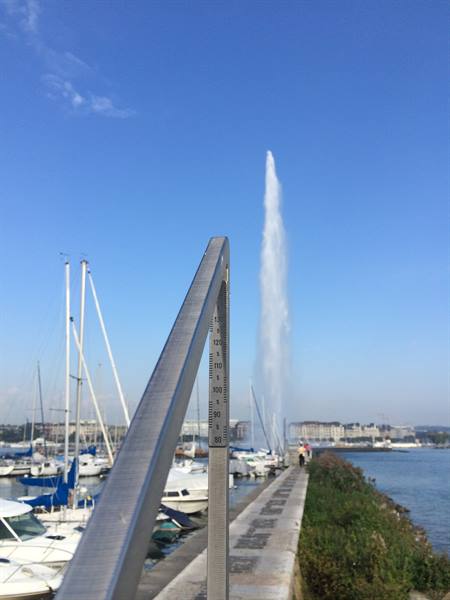 Geneva Jet d'Eau fountain rising above marina sailboats under blue sky