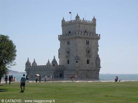 Tourists stroll on the lawn in front of Belém Tower under sunny skies