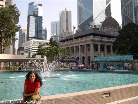 Woman smiling by the Statue Square fountain, with the old Legislative Council building and Hong Kong skyscrapers