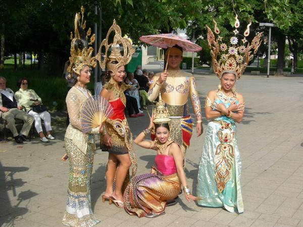 Dancers in golden Thai costumes with tall headdresses posing in a park