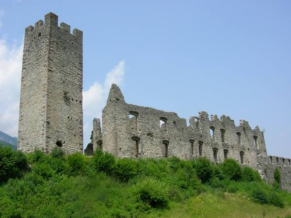 Stone castle ruins with crenellated tower above green bushes, blue sky