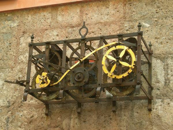 Old wrought-iron clock mechanism with golden gears mounted on a stone wall