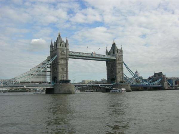 Tower Bridge stone towers over the Thames, boats passing under cloudy sky