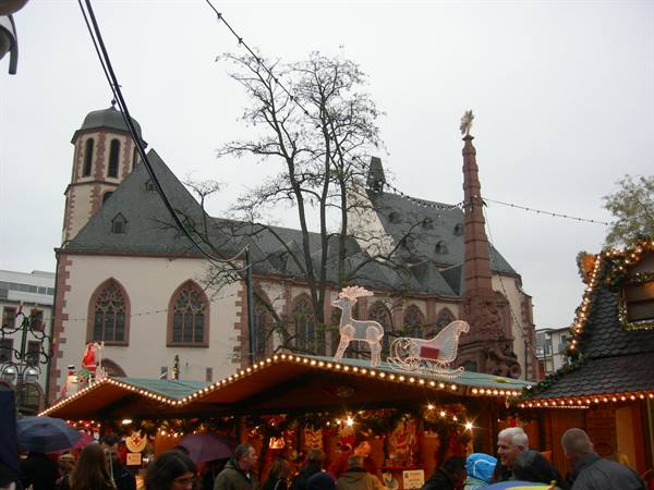 Christmas market in front of Frankfurt's Nikolaikirche, string lights and visitors under umbrellas