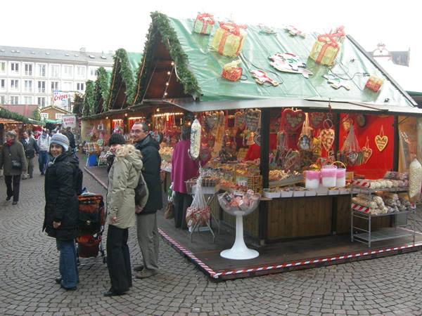 Christmas market stall with sweets and decorations, visitors on cobblestone square