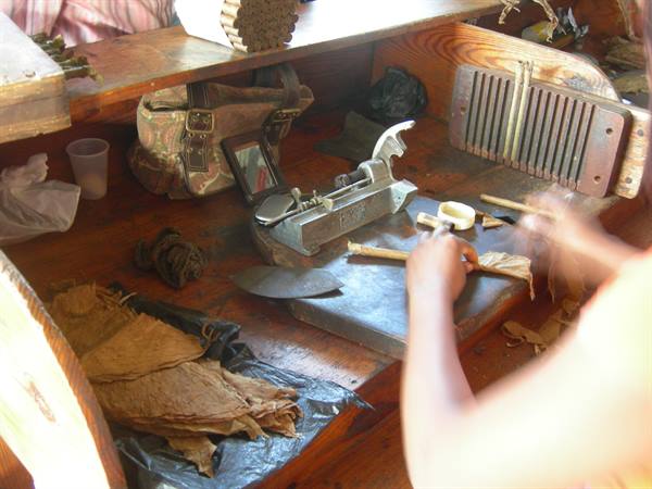 Artisan hand-rolling cigars at wooden workbench with blades and tobacco leaves