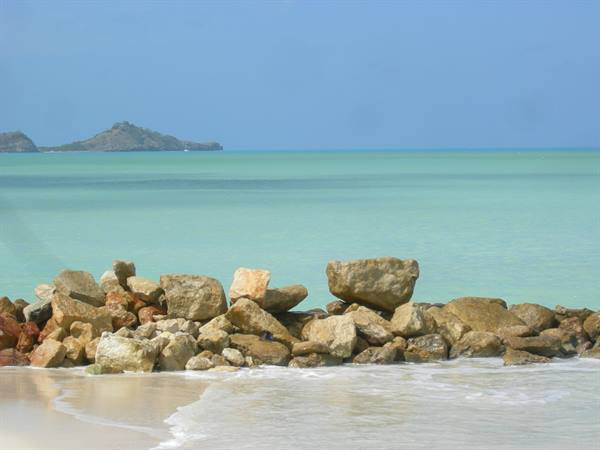 Golden boulders on white sand, turquoise sea and distant islet under blue sky
