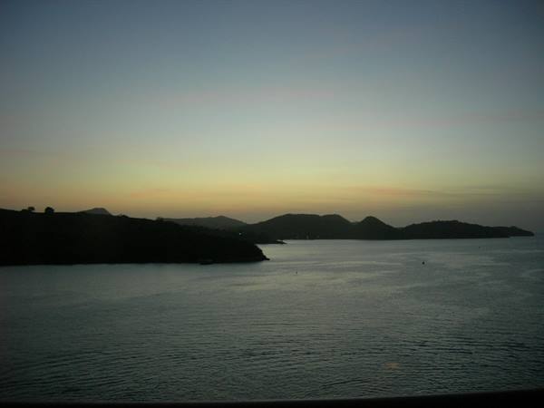 Dark bay with hill silhouettes against golden sky and calm sea at dawn