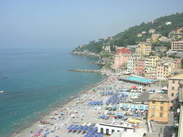 Crowded beach with blue umbrellas between colorful houses and turquoise sea