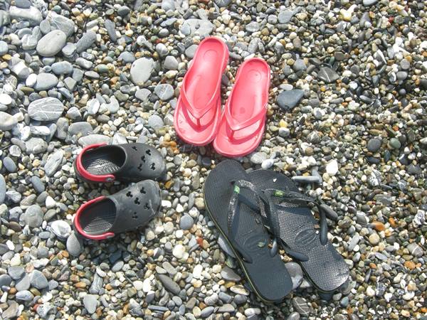 Three pairs of flip-flops and sandals on grey pebble beach