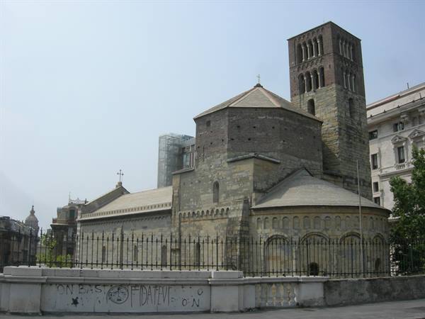 Romanesque stone church with apse and bell tower behind iron fence
