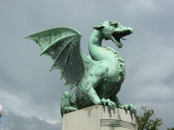 Green copper dragon statue on Ljubljana's Dragon Bridge under cloudy sky