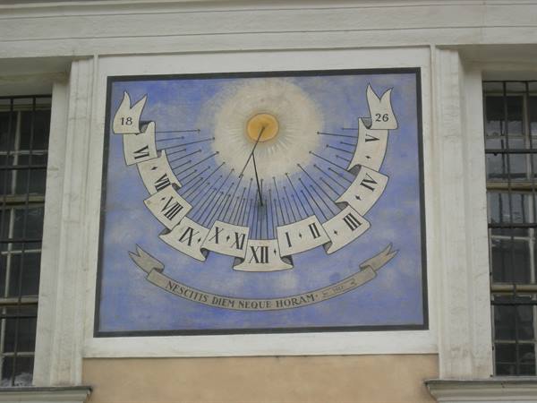 Painted sundial fresco on a facade, with Roman numerals and Latin motto