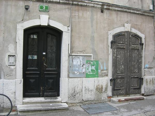 Black wrought iron door and weathered wooden gate on plastered facade, number 3