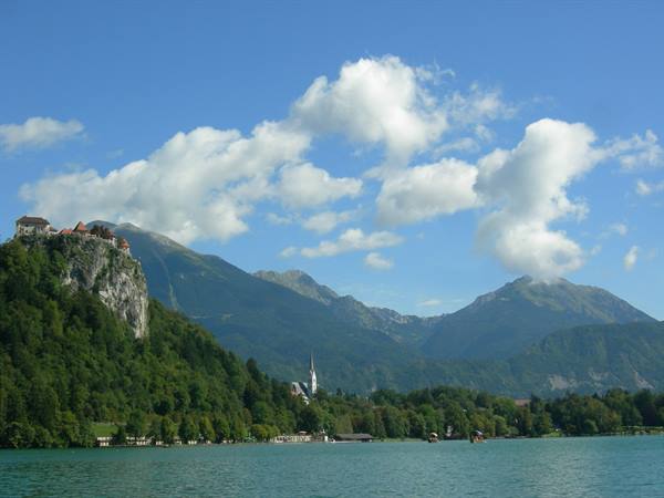 Lake Bled: clifftop castle, white church spire and mountains under clouds