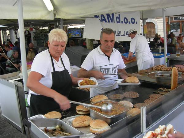 Woman and cook serving grilled meat sandwiches at Ljubljana market stall