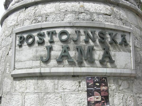 Bronze sign reading Postojnska Jama on the stone facade