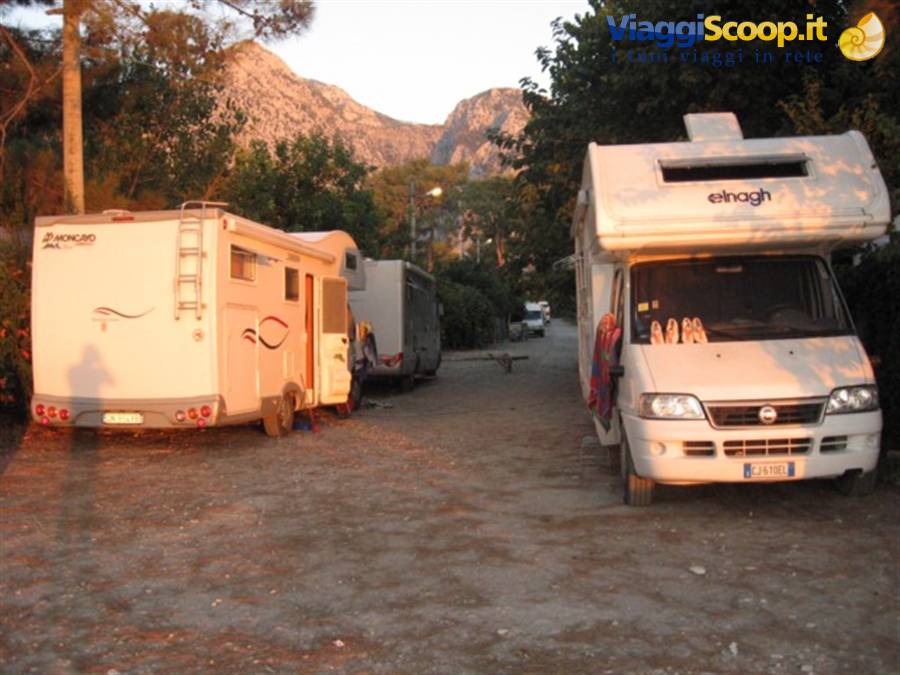 Motorhomes and caravan parked on gravel, mountains glowing at dusk behind