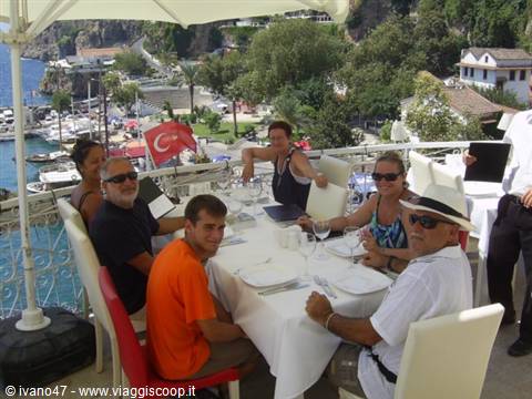 Tourists dining on restaurant terrace, Turkish flag, harbor and houses by the sea