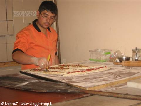 Young pizzaiolo in orange shirt topping pizzas on a floured wooden table