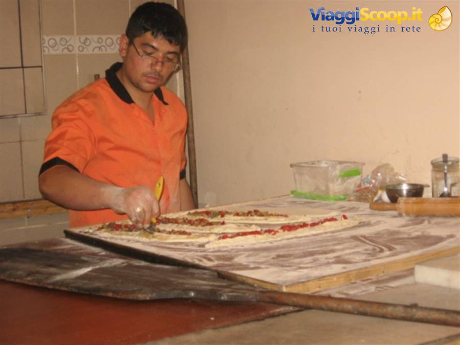 Young pizzaiolo in orange shirt topping pizzas on a floured wooden table