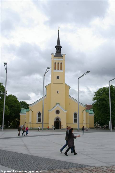 Yellow St. John's Church in Tallinn, people crossing the square under cloudy sky