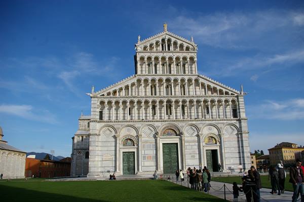 Marble facade of Pisa Cathedral, tourists on the path under blue sky