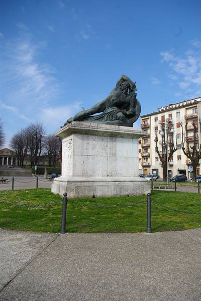 Bronze statue on marble base in a grassy square among buildings