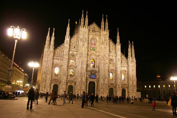 Milan Cathedral lit up at night, people strolling across the square