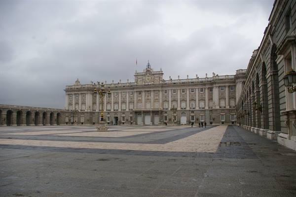 Royal Palace of Madrid, stone facade under grey sky, empty wet square
