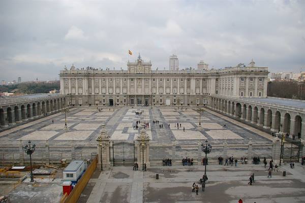 Royal Palace of Madrid, stone facade under cloudy sky, tourists in the square