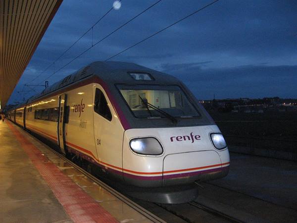 Renfe train stopped at the station platform at night, headlights on