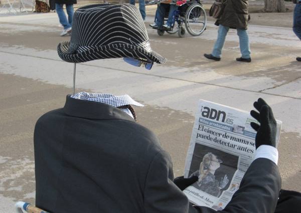 Invisible man statue in striped hat reads ADN newspaper on a plaza