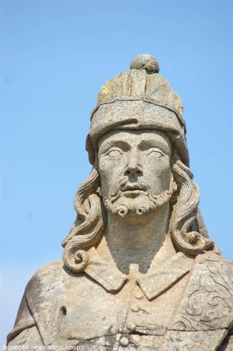 Stone statue of a crowned man with long hair against blue sky