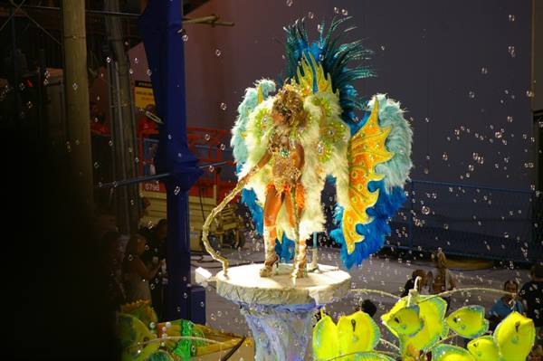 Dancer in blue and yellow feathered carnival costume on parade float