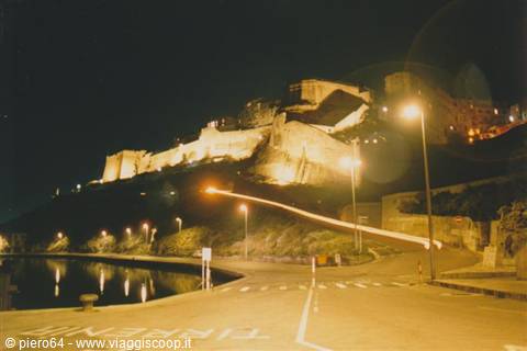 Illuminated castle at night above the road and harbor