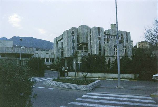 Brutalist concrete building behind a fence, empty road crossing and grey mountains