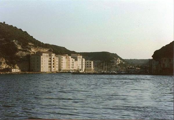 pale buildings along Bonifacio harbor beneath limestone cliffs, boats moored