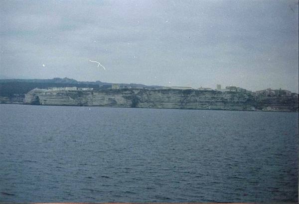 Limestone cliffs topped by houses seen from the sea, overcast sky