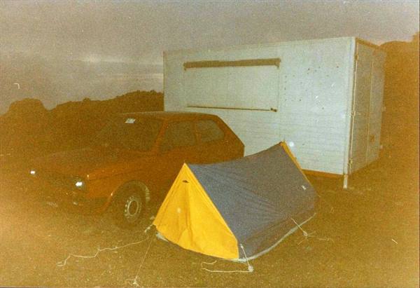 Yellow and blue tent beside a red car and a white trailer