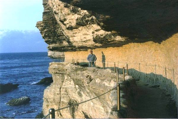 Man in blue sweater on rocky path above the sea, under limestone cliff