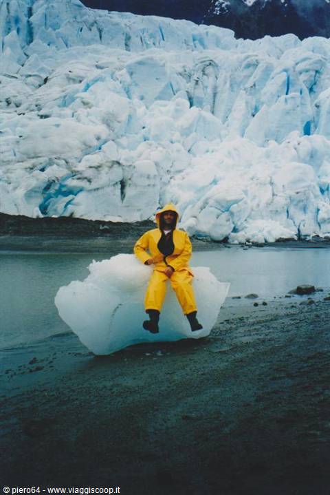 Man in yellow rain suit sitting on an ice block before a glacier