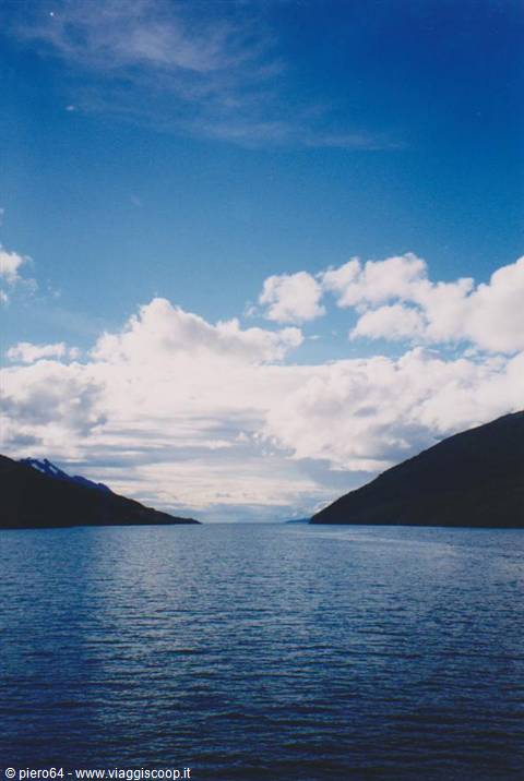 Dark waters between snowy mountains under white clouds, Patagonian fjord
