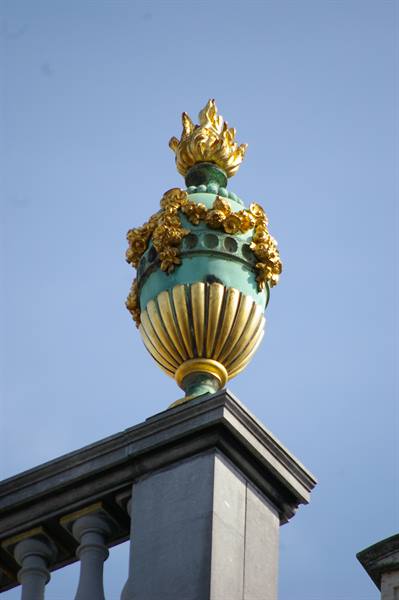 Gilded verdigris urn with golden flame atop a grey stone balustrade