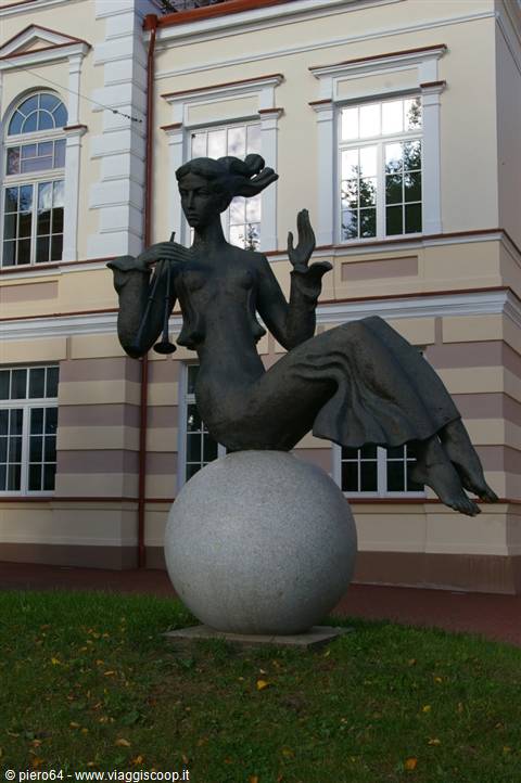 Bronze statue of a woman musician sitting on a granite sphere by a pale building