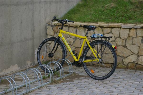 Yellow bicycle parked on metal bike rack next to stone wall