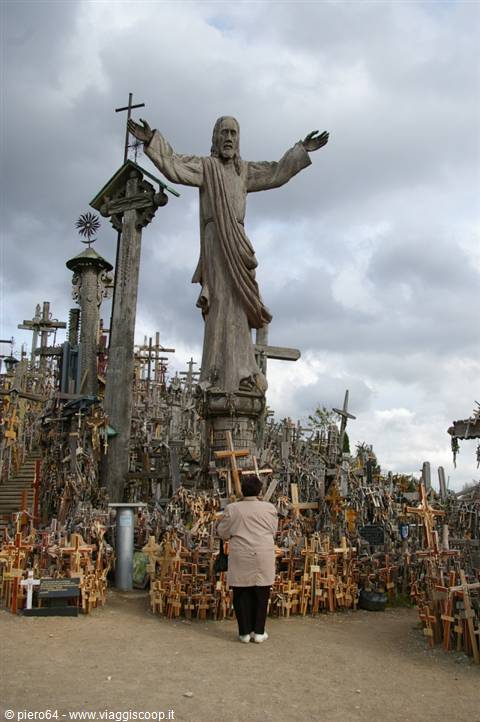 Hill of Crosses: Christ statue among thousands of wooden and metal crosses, visitor watching